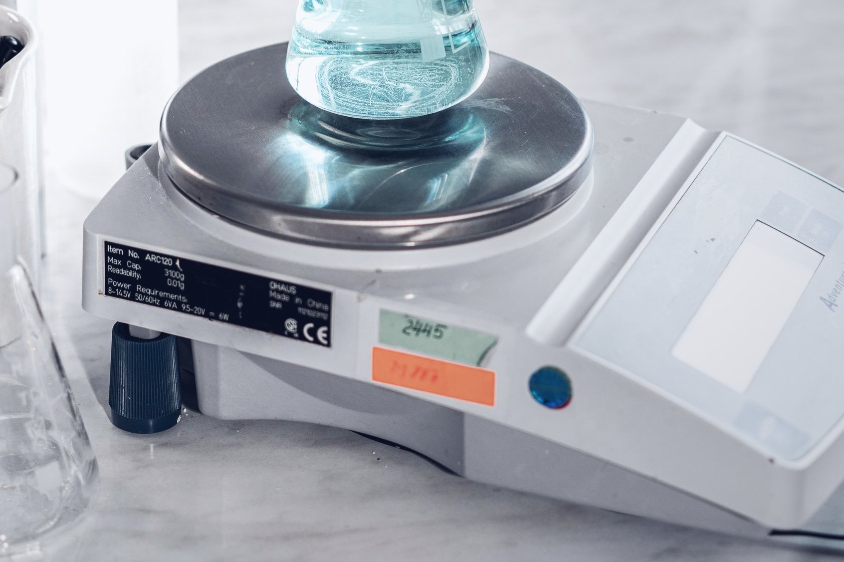A flask of clear solution on the pan of an analytical balance.